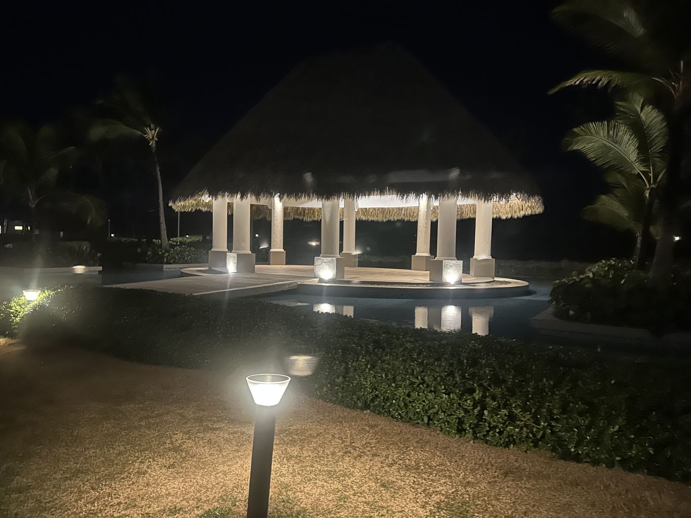 Illuminated thatched gazebo reflected in a resort pool at night