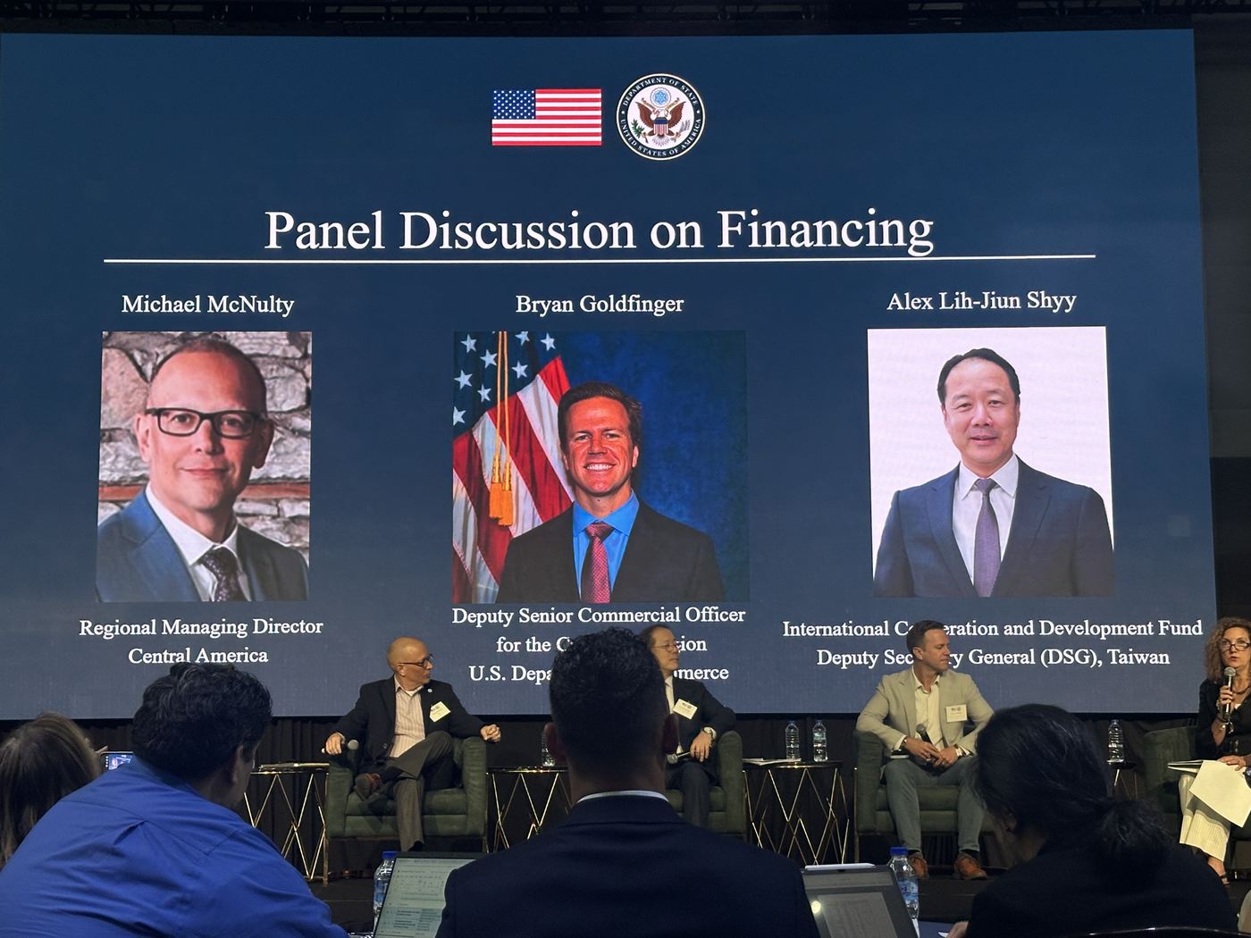 Four panellists on stage beneath a slide introducing the financing panel
